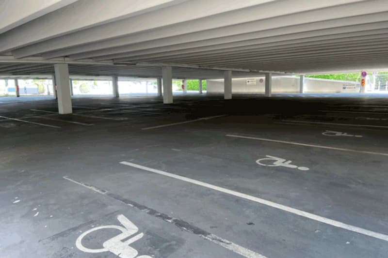 Leeres überdachtes Parkdeck mit markierten Behindertenparkplätzen und Stützpfeilern.