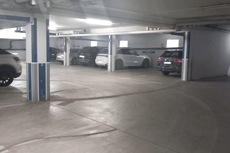 Tiefgaragenebene mit Betonboden, Stützpfeilern und mehreren geparkten Autos entlang der Wand.
