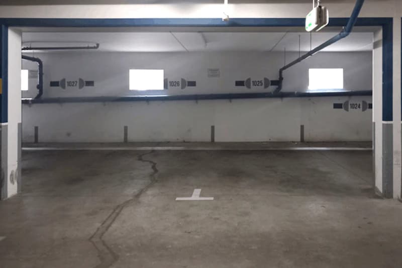 Leerer Parkbereich in Tiefgarage mit Bodenmarkierung, Pfeilnummern 1024–1027 an der Wand und kleinen Fensteröffnungen.