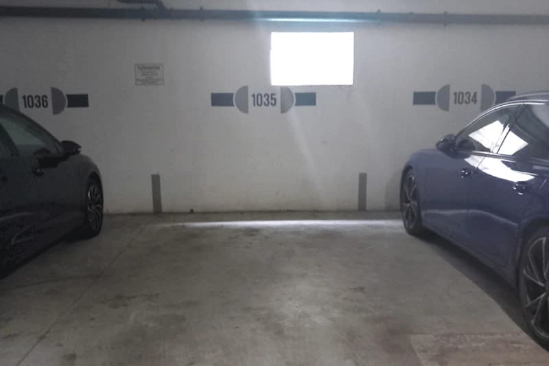Freier Parkstand Nummer 1035 in einer Tiefgarage zwischen geparkten Autos und kleinem Fenster an der Wand.