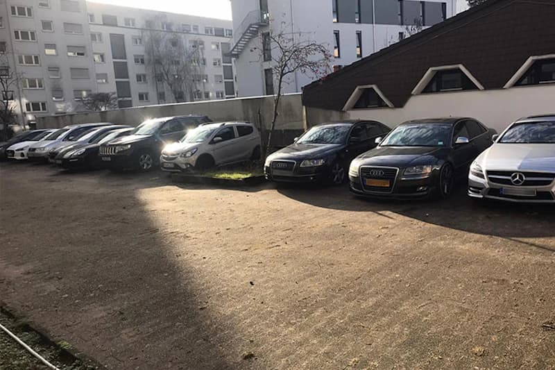 Reihe geparkter Autos auf befestigtem Parkplatz neben Wohngebäuden.