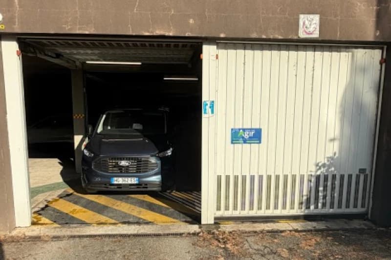 Auto steht in geöffneter Einfahrt einer Parkhalle, weiße Schiebetür mit Agir-Schild sichtbar.
