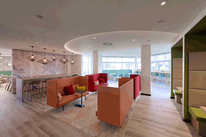 Moderne Hotellounge mit farbigen Sitznischen, Sofas, hohen Tischen und großen Fenstern.
