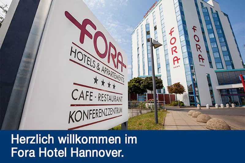 Schild mit FORA Schriftzug im Vordergrund und mehrstöckiges Hotelgebäude im Hintergrund.