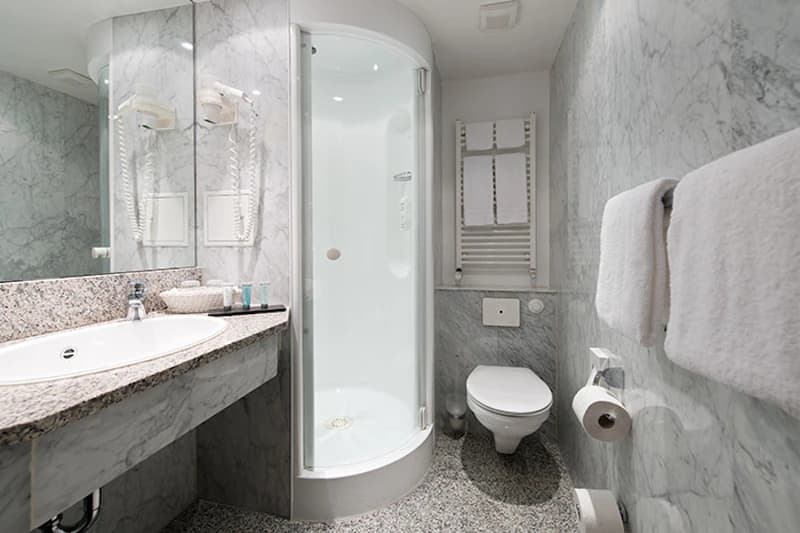 Kompaktes Badezimmer mit abgerundeter Glasdusche, Waschbecken, großem Spiegel, Wandtoilette und Handtüchern.