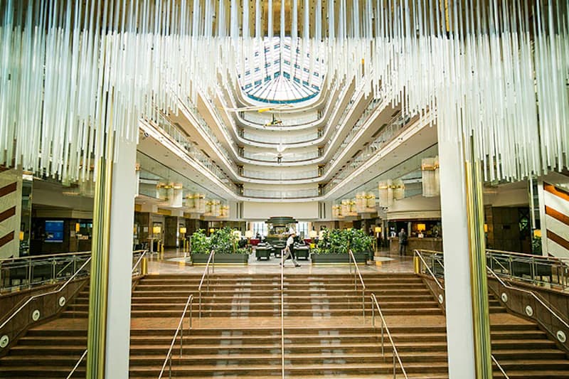 Große Hotellobby mit breiter Treppe, mehrstöckigen Balkonen und zentralem Oberlicht.