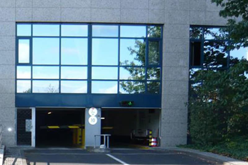 Einfahrt zur Tiefgarage unter einem Gebäude mit großflächigen Fenstern, zwei Durchfahrten und Verkehrsschild 10.