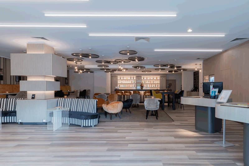 Hotel-Lobby mit Sitzgruppen, Bar im Hintergrund und Rezeption rechts.