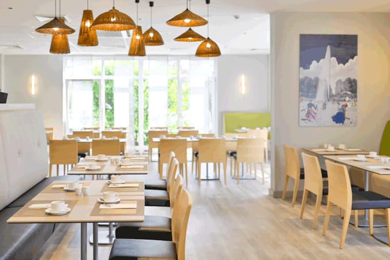 Helles Hotelrestaurant mit Reihen von Tischen, gedeckten Kaffeetassen und geflochtenen Hängeleuchten.