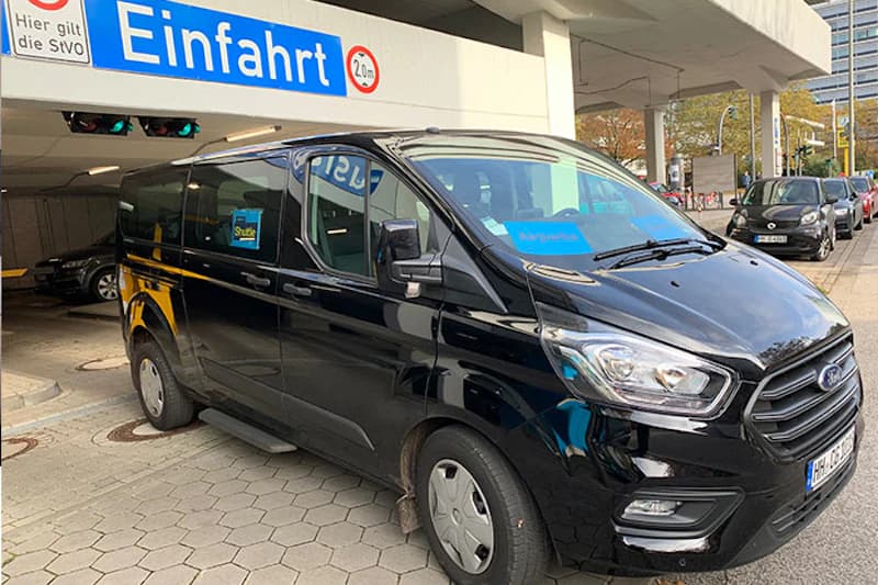 Schwarzer Kleinbus vor Parkhauseinfahrt mit Schild Einfahrt und Höhenbegrenzung 2,0 m.
