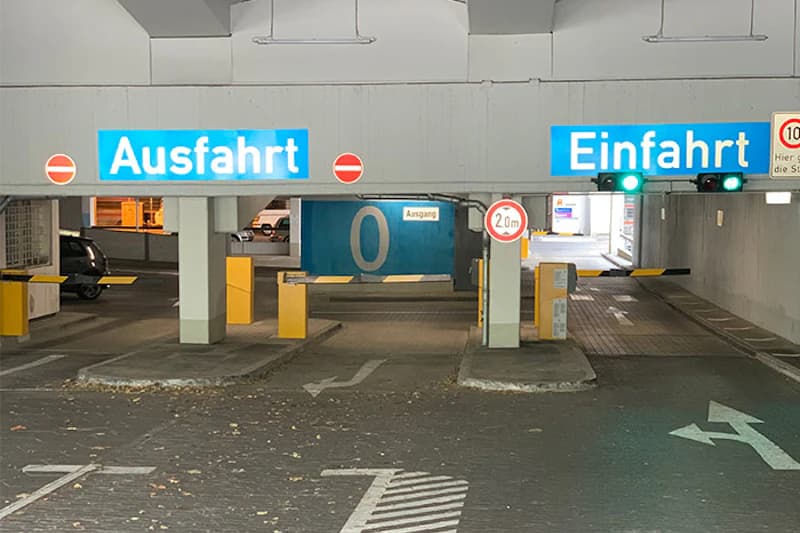 Einfahrt und Ausfahrt eines Parkhauses mit Schranken, grünen Ampeln und Schild Höhenbegrenzung 2,0 m.