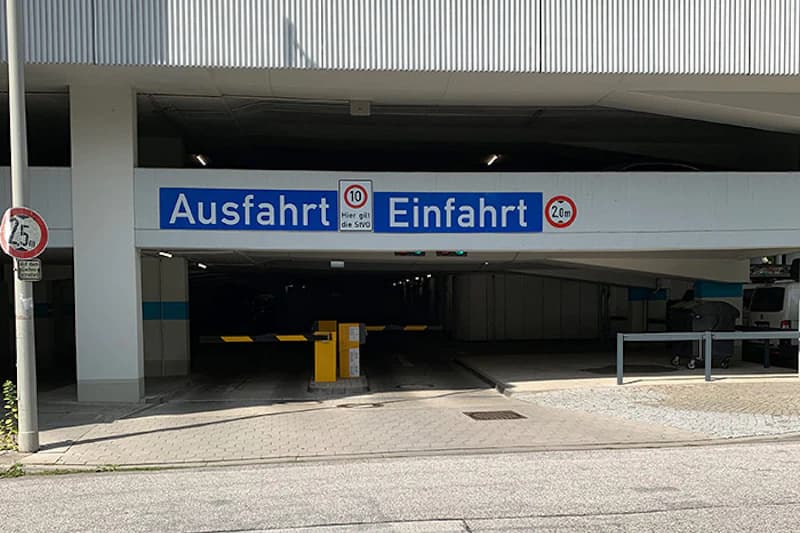 Parkhauszufahrt mit gelber Schranke, blauem Ausfahrt und Einfahrt Schild und Höhenbegrenzung 2,0 m.