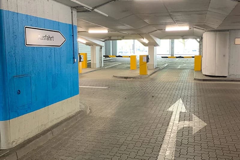 Innenansicht Parkhaus mit blauem Pfeilschild Ausfahrt, Fahrbahnmarkierung und gelben Schranken.