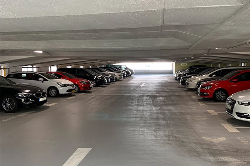 Parkdeck in einem Parkhaus mit geparkten Autos links und rechts und mittiger Fahrspur unter niedriger Decke.