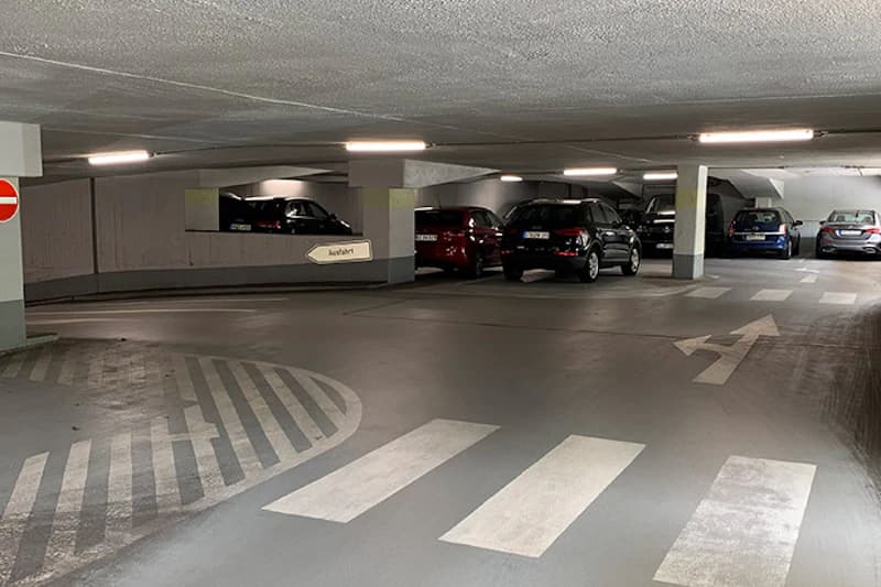 Tiefgarage mit mehreren geparkten Autos, Stützpfeilern, Bodenmarkierungen und Schild Ausfahrt.