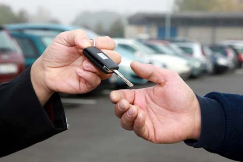 Hand reicht Autoschlüssel an andere Hand vor geparkten Autos.
