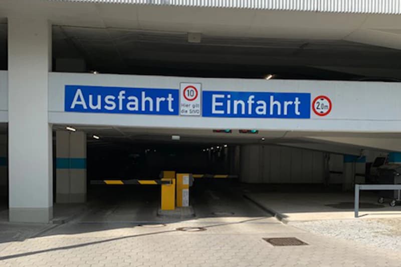 Tiefgarageneinfahrt mit Schranke und blauem Ausfahrt Einfahrt-Schild sowie Höhen- und Tempobegrenzung.