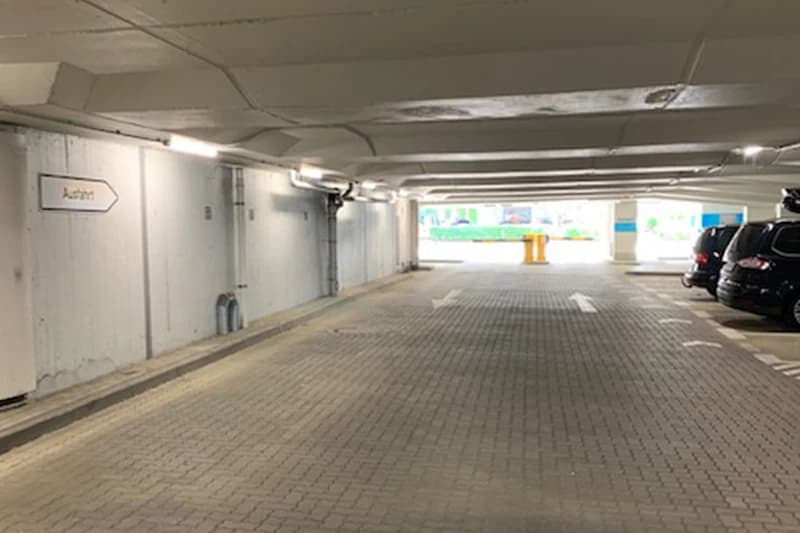 Tiefgaragenebene mit Fahrbahnmarkierungen, Pfeilen, Wegweiserschild Ausfahrt und geparkten Autos rechts.