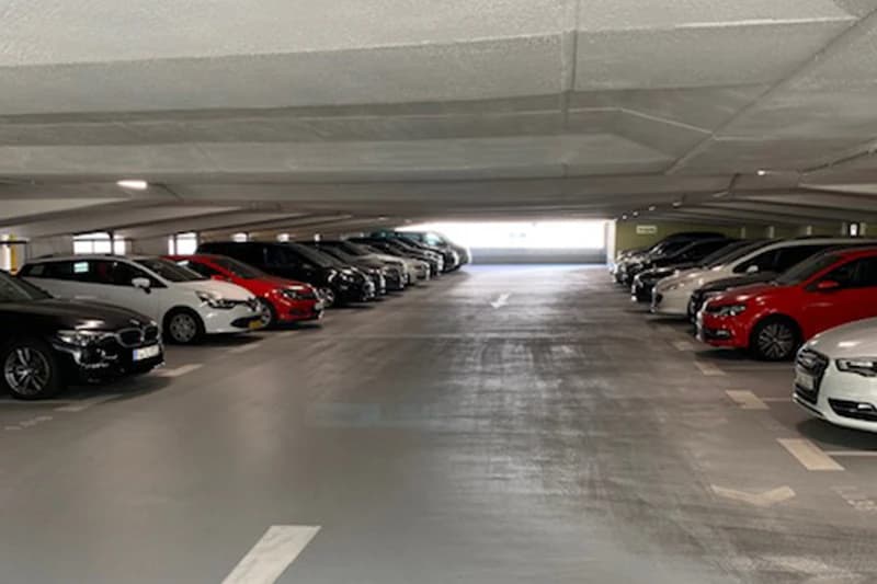 Parkdeck mit geparkten Autos auf beiden Seiten und freier Fahrspur zur hellen Ausfahrt.