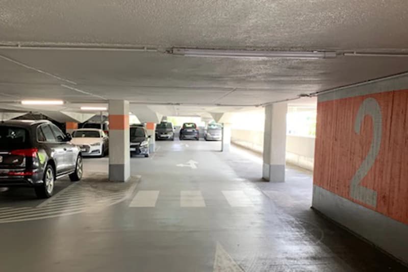 Überdachtes Parkdeck mit geparkten Autos, Stützpfeilern, Fußgängerstreifen und roter Wandmarkierung 2.