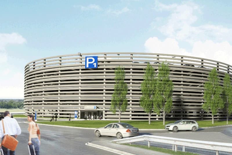 Rundes Parkhaus mit P1-Schild, Fahrzeugen, Passanten mit Gepäck und Bäumen vor dem Terminal.