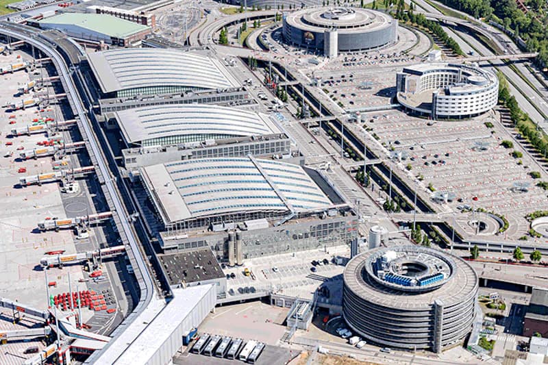 Luftaufnahme des Hamburger Flughafens mit mehreren Terminalhallen, runden Parkhäusern und großen Parkflächen.