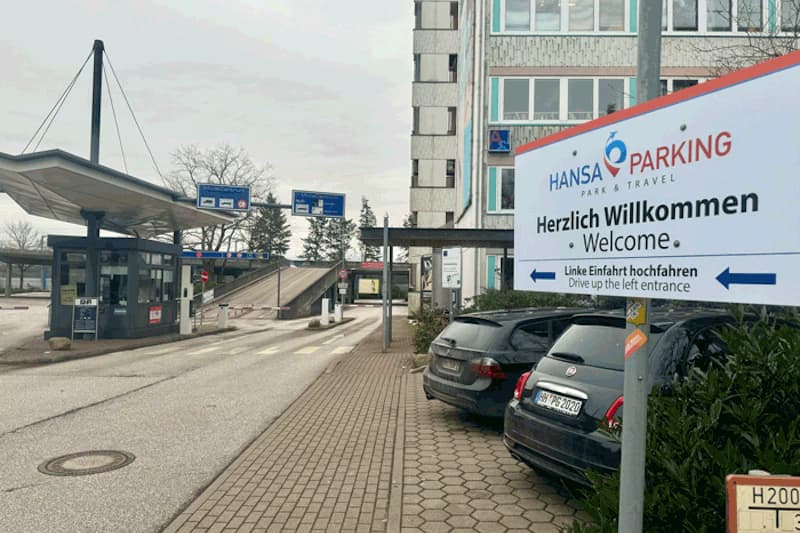 Einfahrt zum Hansa Parking mit Willkommensschild, Parkhäuschen, Rampenauffahrt und geparkten Autos.
