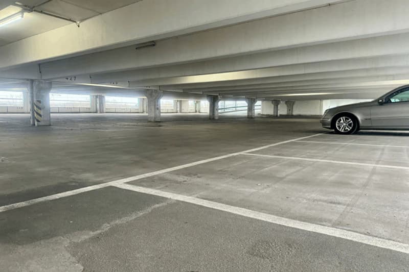 Leeres mehrgeschossiges Parkhaus mit Betonstützen, markierten Stellplätzen und silbernem Auto rechts.