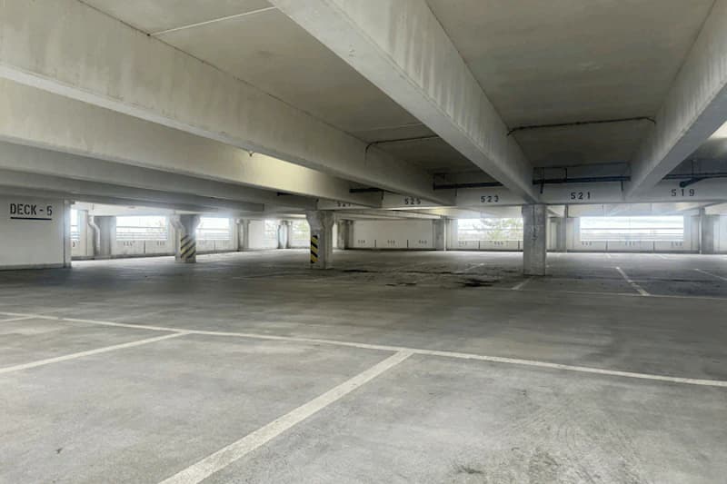Leeres Betonparkdeck Ebene 5 mit markierten Stellplätzen, Stützpfeilern und Licht durch Wandöffnungen.