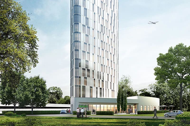 Runder Hotelturm mit niedrigem Anbau, Bäume davor, mehrere Fußgänger, Autos und ein Flugzeug am Himmel.