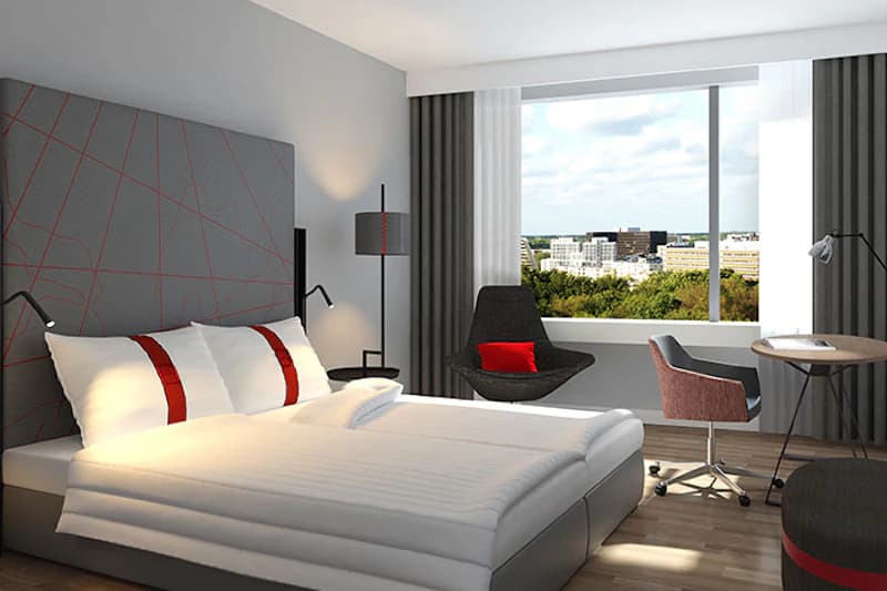 Modernes Hotelzimmer mit Doppelbett, großem Fenster, Sessel, Schreibtisch und Stadtblick.