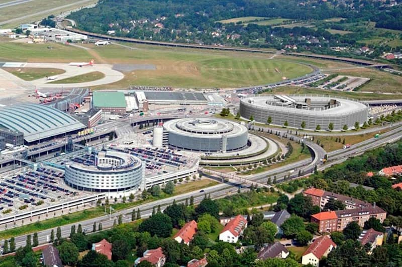 Luftaufnahme des Hamburger Flughafens mit mehreren runden Parkhäusern, Terminal, Flugzeug und Rollfeld.