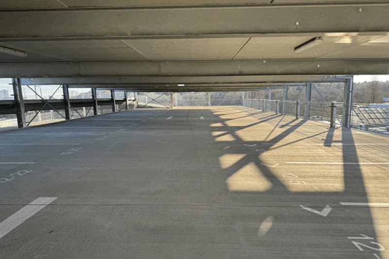 Leerer Parkhauslevel mit nummerierten Stellflächen, Betonboden, Metallgeländer und langen Schatten.