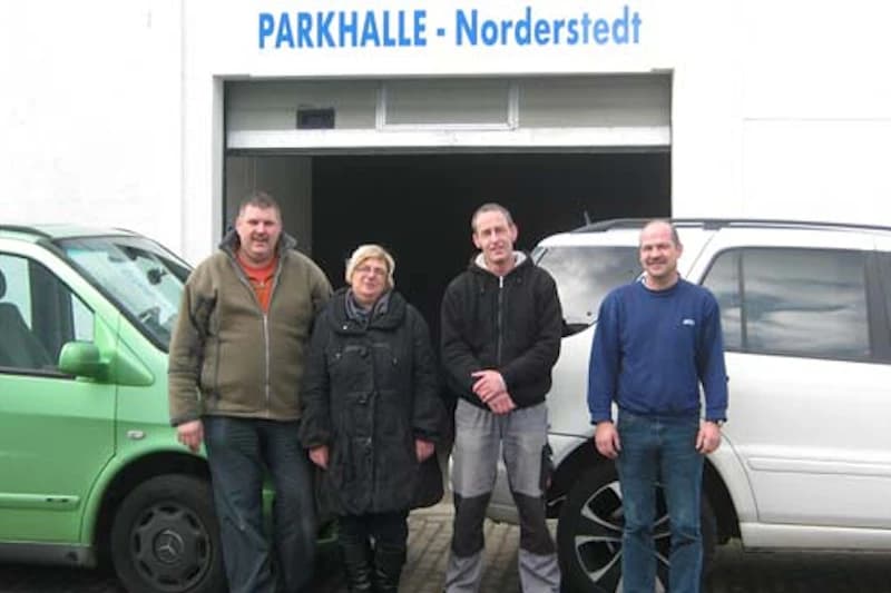 Vier Personen stehen vor der Einfahrt zur Parkhalle Norderstedt zwischen zwei Fahrzeugen.