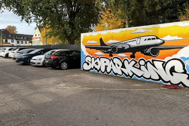 Reihe geparkter Pkw neben einer bemalten Mauer mit Flugzeugmotiv und Schrift SKYPARKING.