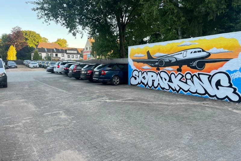 Parkplatz mit geparkten Autos neben Wandgraffiti eines Flugzeugs und Schriftzug SKYPARKING.