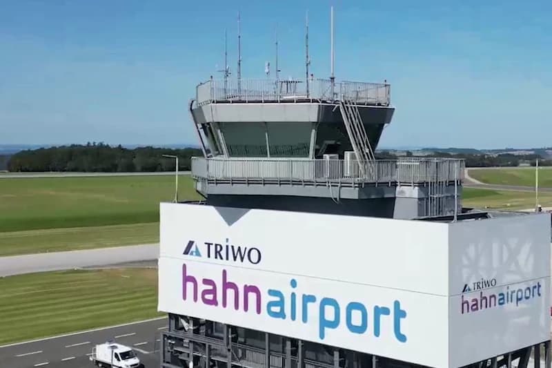 Kontrollturm mit grossem hahnairport-Logo und TRIWO-Schriftzug, Rollfeld im Hintergrund und weisser Lieferwagen an der Zufahrtsstrasse.