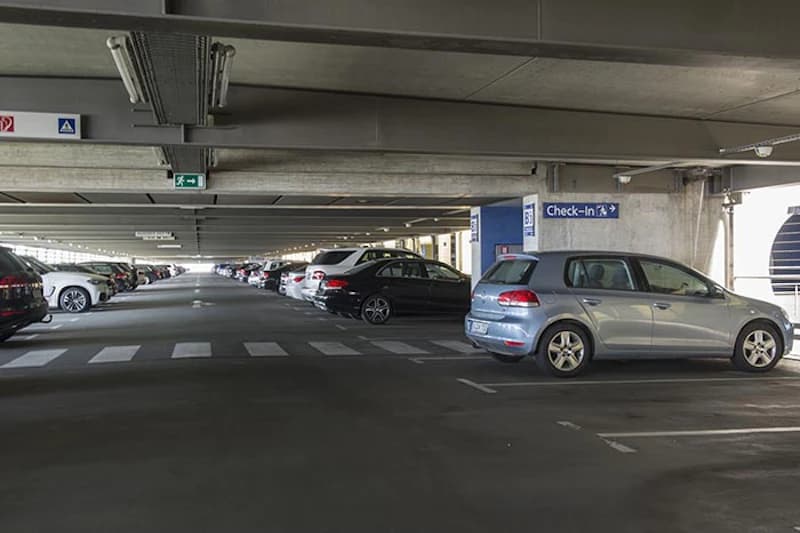 Parkhausinnenraum mit Reihen geparkter Autos, Zebrastreifen und Schild Check-In.