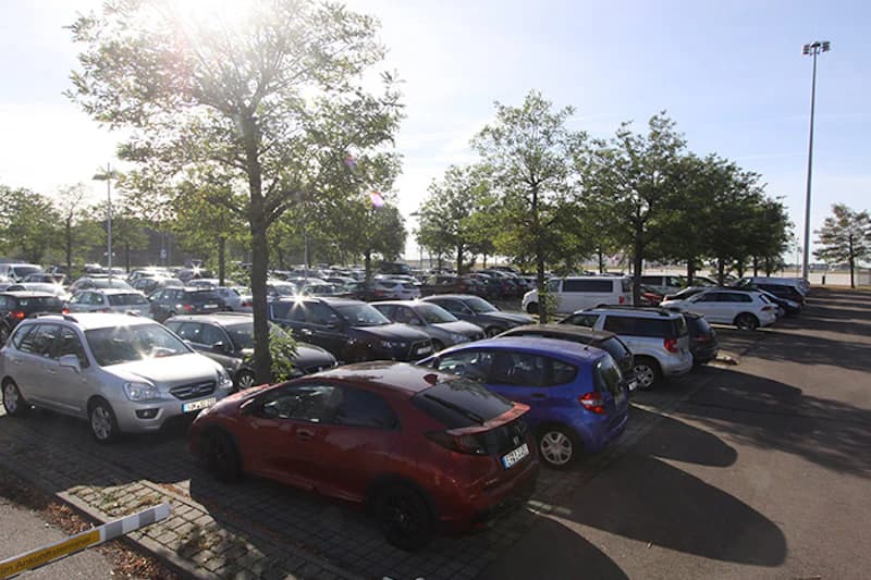 Voller Außenparkplatz mit Reihen geparkter Autos und Bäumen bei sonnigem Himmel.