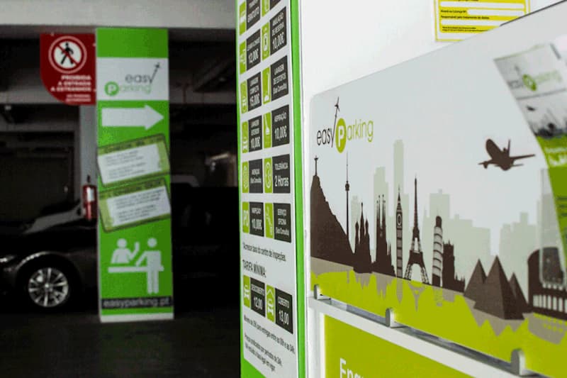 Parkhausgang mit Easy Parking Informationstafel, grünen Säulen, Piktogrammen und einem geparkten Auto im Hintergrund.