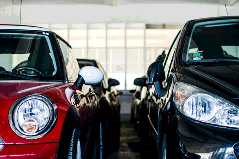 Enge Parkreihe in beleuchteter Parkhalle mit rotem Kleinwagen links und schwarzem Wagen rechts.