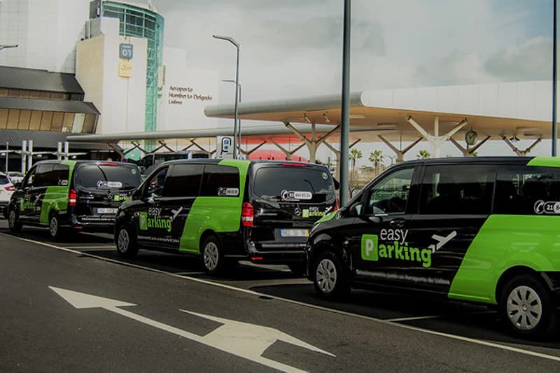 Mehrere schwarz-grüne Easy Parking Shuttlefahrzeuge in einer Reihe am Abholbereich des Flughafens Lissabon.
