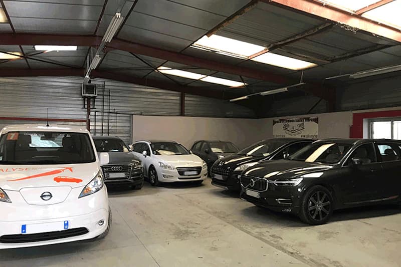 Überdachte Parkhalle mit mehreren nebeneinander geparkten Autos, vorne links ein weißer Van mit Alyse-Logo.