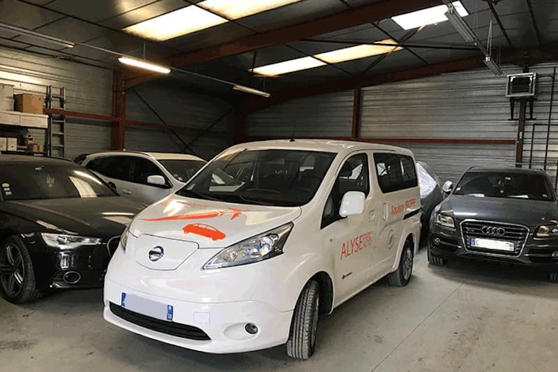 Weißer Alyse-Service-Van mit orangefarbenem Logo in einer beleuchteten Parkhalle zwischen geparkten Pkw.
