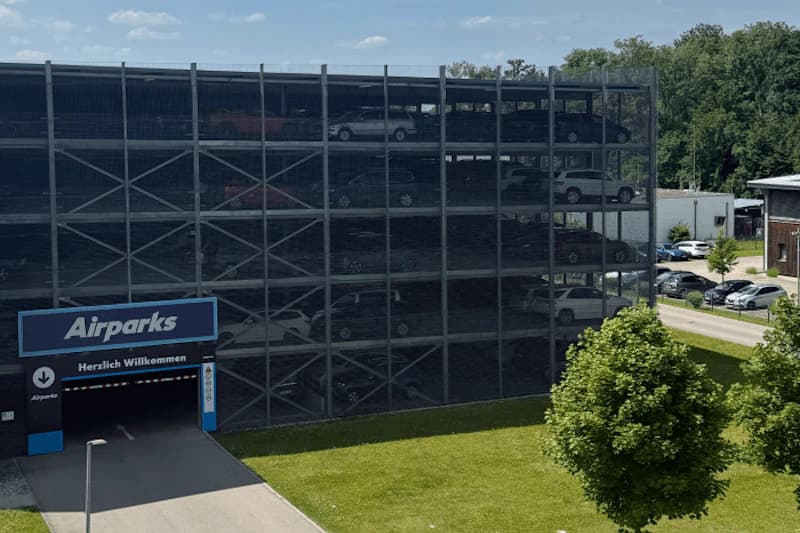Mehrstöckiges Parkhaus mit Gitternfassade, sichtbar geparkte Autos und blaues Airparks-Schild über der Einfahrt.