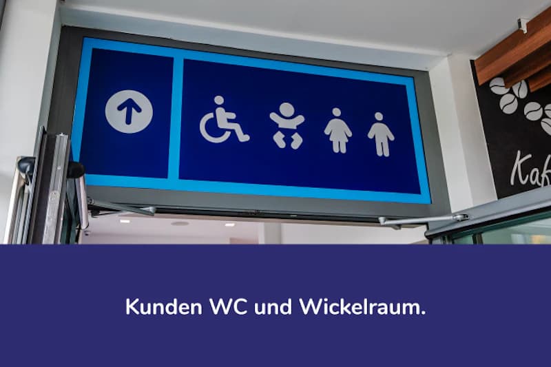 Blaues Leitschild mit Pfeil nach oben und Symbolen für Rollstuhl, Wickeltisch, Damen und Herren.