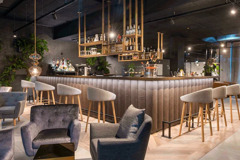 Hotelbar mit Tresen, Barhockern, Sitzsesseln und hängenden Regalen mit Flaschen.