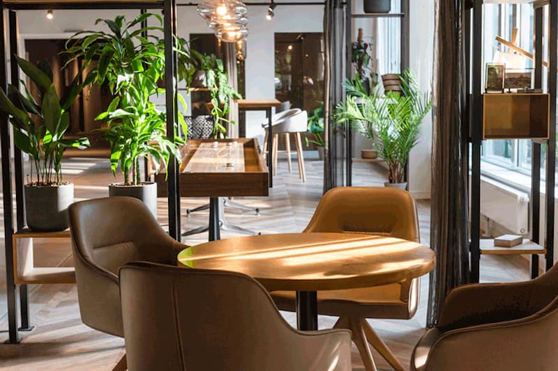 Runder Holztisch mit vier braunen Sesseln in einer Hotel-Lounge, Pflanzen und Regale im Hintergrund.