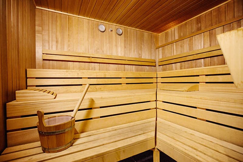 Holzsauna mit mehrstufigen Sitzbänken, Holzeimer und Aufgusskelle sowie Thermometern an der Wand.