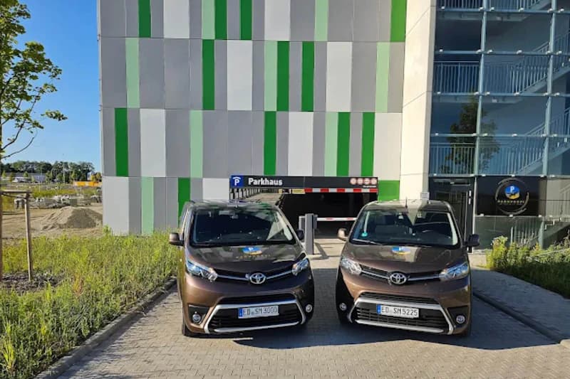 Zwei braune Dienstwagen stehen vor der Einfahrt zum Parkhaus mit grün-grauer Fassadenverkleidung und Parkhaus-Schild.